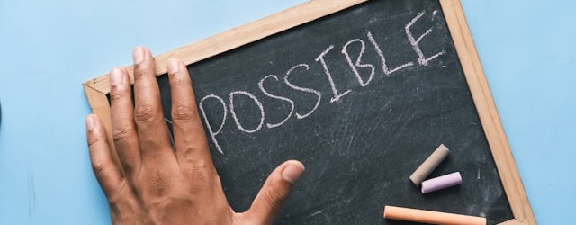 Hand on a chalkboard with the word “Possible” written in chalk signifying possibility of improved marketing process
